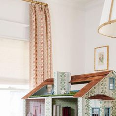 a doll house is sitting on a table in front of a window with curtains and drapes