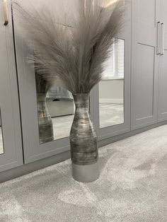 a vase with feathers in it sitting on the floor next to some cupboards and mirrors