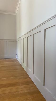 an empty room with white walls and wood flooring in the foreground, there is no one on the far wall