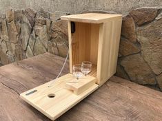 a wooden box with two wine glasses in it sitting on a table next to a stone wall