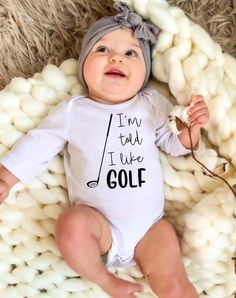 a baby laying on top of a pile of balls wearing a white bodysuit with the words i'm too cute to be golf