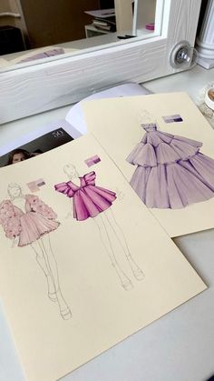 three paper drawings of dresses on top of a table