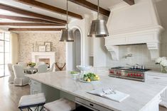 a large kitchen with white cabinets and marble counter tops, along with two pendant lights hanging from the ceiling