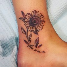 a sunflower tattoo on the foot with words written in cursive writing below it