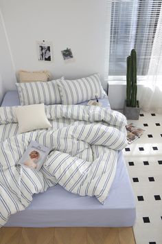 an unmade bed with blue and white striped comforter, pillows and pictures on the wall