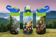 three water bottles with dinosaurs on them and mountains in the background