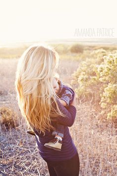 a woman is standing in the grass with her back to the camera and she has long blonde hair