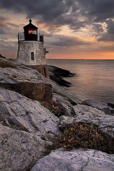 a light house sitting on top of a rocky cliff next to the ocean at sunset