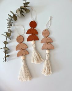 three wooden pieces with tassels hanging from them on a white surface next to plants