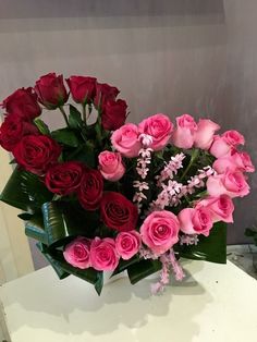 a vase filled with pink and red roses on top of a white table next to a plant