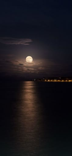 the full moon is seen over the ocean at night with clouds in the sky and water