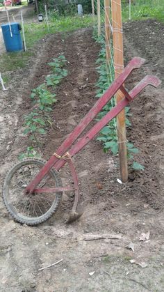 an old bicycle leaning against a pole in the dirt near a tree and fence post