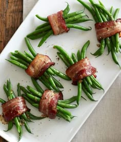 green beans and bacon wrapped in bacon on a white platter with a wooden table