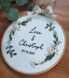 a white embroidered wedding ornament with flowers and greenery on the front, hanging from a wooden hoop