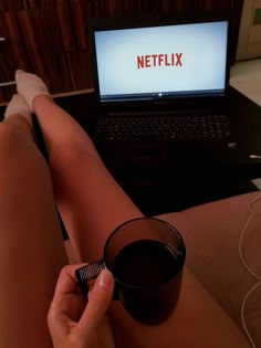 a person is holding a glass in front of a laptop with the netflix logo on it