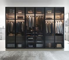 a walk in closet filled with clothes next to a large wall mounted mirror and light fixture