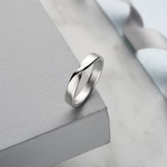 a silver ring sitting on top of a piece of wood next to a white wall