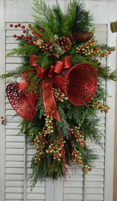 a christmas wreath with pine cones, berries and red ribbon hanging on a white door