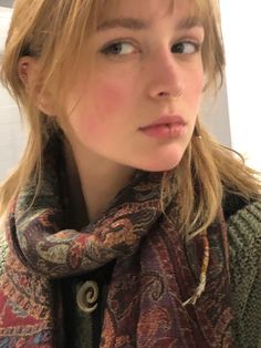 a close up of a person wearing a scarf and looking at the camera with a serious look on her face