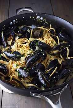 a pan filled with pasta and mussels on top of a wooden table