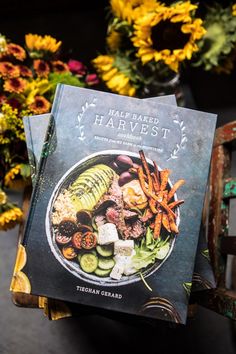 two cookbooks are stacked on top of each other in front of some colorful flowers