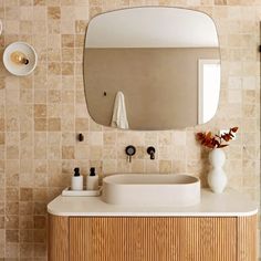 a bathroom sink sitting under a mirror next to a white vase with flowers in it