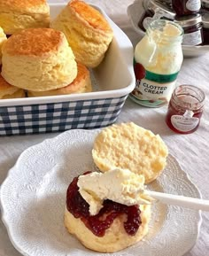 biscuits, jam and butter on a plate next to a bowl of biscuits with cream