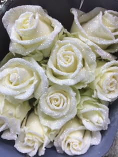 a bunch of white roses sitting in a blue bowl with water droplets on the petals