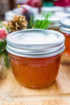 three jars filled with honey sitting on top of a wooden table next to pine cones