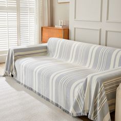 a couch covered in a striped blanket next to a window with shutters on both sides