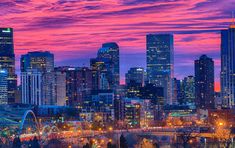 the city skyline is lit up at night with bright lights in the sky and colorful clouds