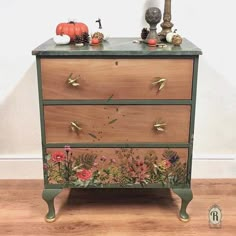 an old dresser with flowers and leaves painted on it's sides, sitting on a wooden floor