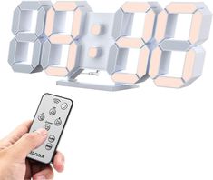 a hand holding a remote control in front of a clock made out of cubes