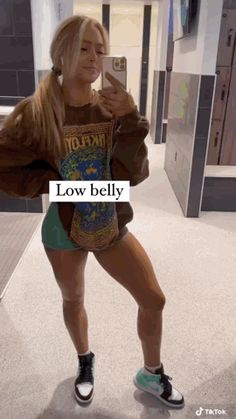 a woman taking a selfie with her cell phone in an airport hallway while wearing shorts and sneakers