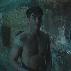 a shirtless man standing in front of a cave