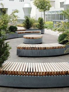 an outdoor seating area with wooden benches and trees in the background, surrounded by concrete planters