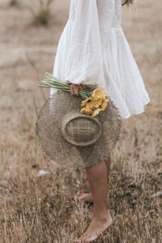 a woman in a white dress holding a straw hat and flowers