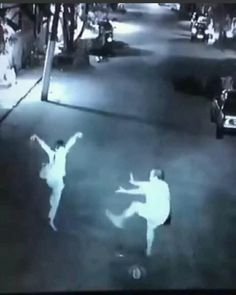 two people are dancing in the street at night time, one is holding his arms up