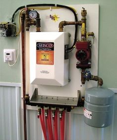 a tank mounted to the side of a wall next to a water heater and pipes