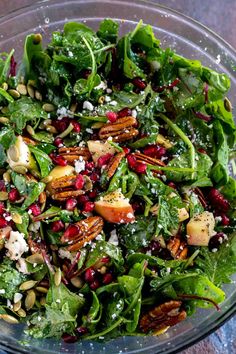 a salad in a glass bowl with nuts, spinach and pomegranate