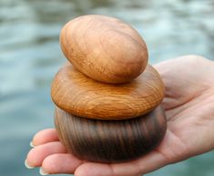 a person is holding three wooden rocks in their hand by the water's edge