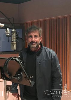 a man is standing in front of a microphone and recording equipment, with the sound board behind him