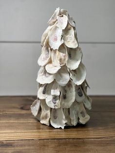 a white christmas tree made out of seashells on a wooden table with a gray wall in the background