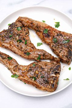 three steaks on a white plate with parsley sprinkled around the edges