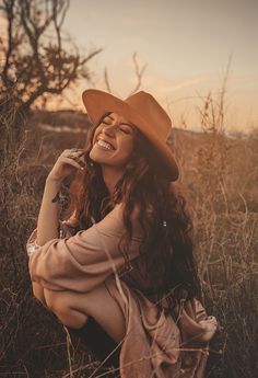 a woman wearing a cowboy hat sitting in tall grass