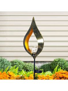 a lamp that is in the middle of some flowers and grass with a house in the background