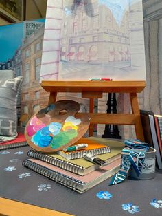 an easel with paint, books and other art supplies on top of a table