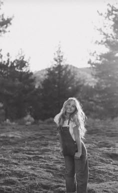 black and white photograph of a woman in overalls posing for the camera with trees in the background