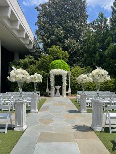 an outdoor ceremony set up with white flowers and greenery on the aisle, surrounded by chairs