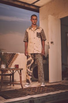 a man standing in front of an open door wearing patterned pants and a white shirt